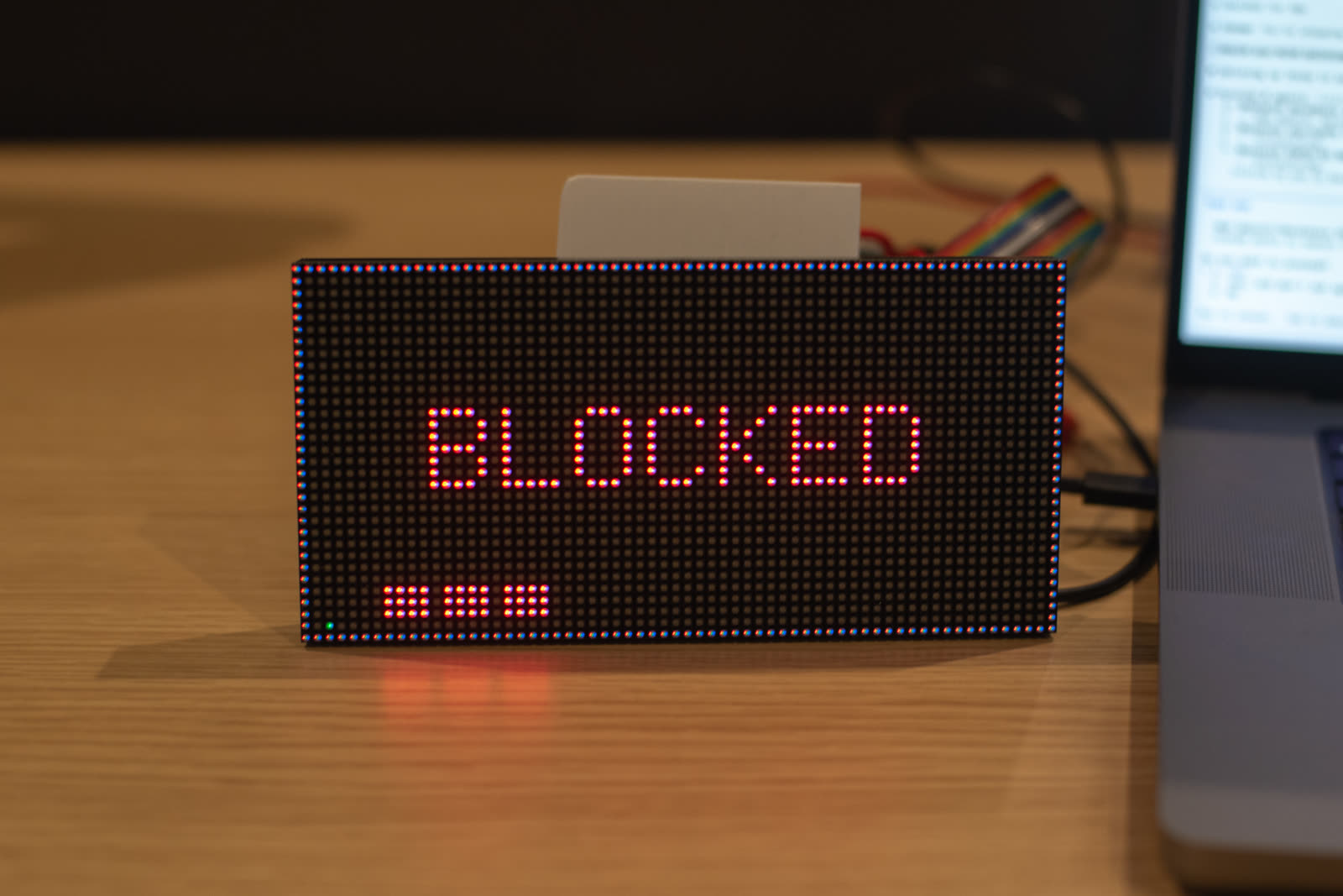 The panel showing BLOCKED in red dot-matrix letters with a red-and-blue alternating border — the agent is waiting on a permission prompt. Small dot clusters along the bottom edge show activity counters.